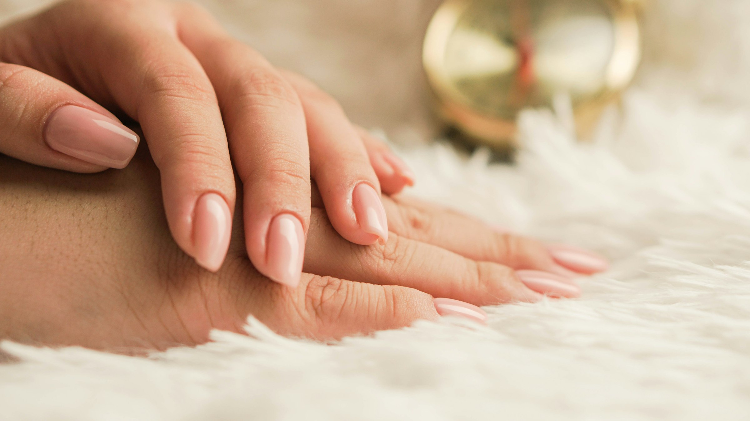 Hands with soft nude nails resting on a cream throw